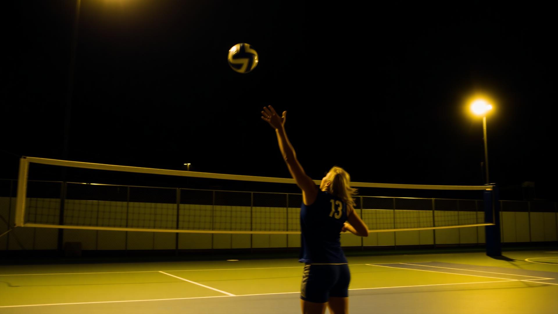 Jogadora sacando durante partida de vôlei noturna